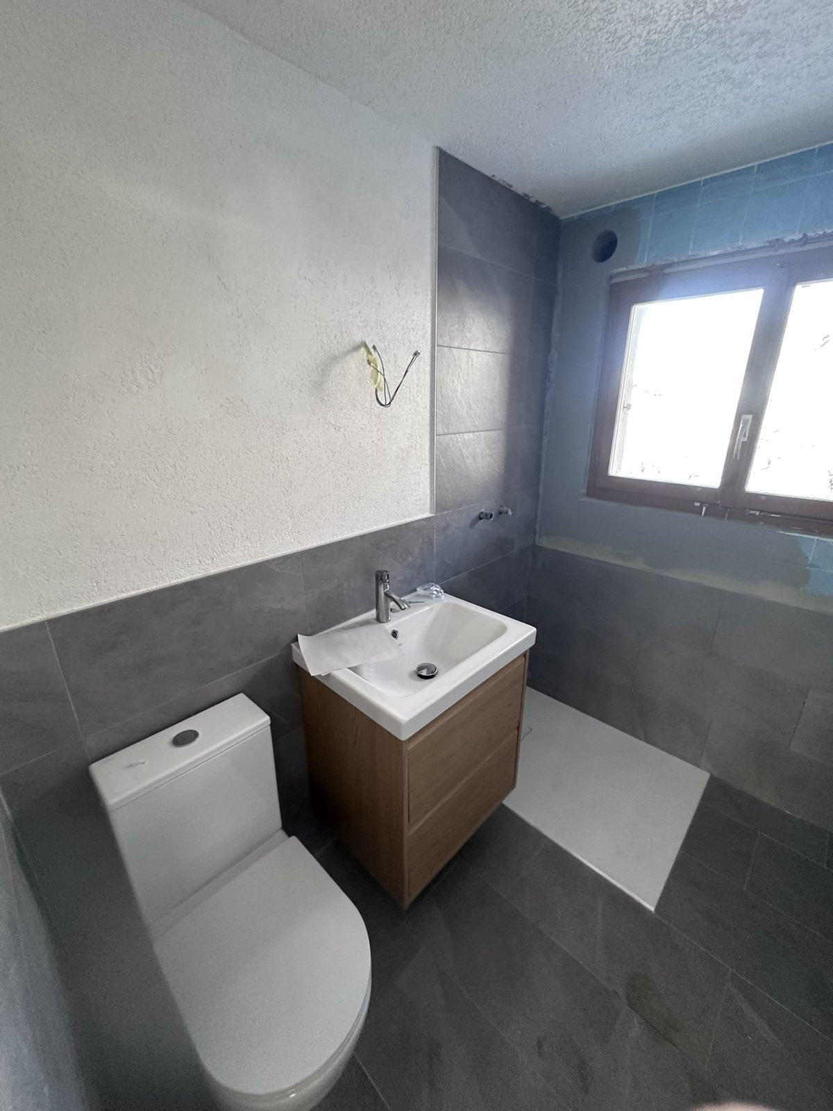 Fertiges Badezimmer im Chalet Harmonie mit grossformatigen Platten in Anthrazit und Holz-Waschtisch